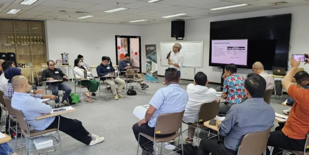 Peserta pelatihan duduk melingkar menyimak fasilitator yang memimpin sesi di depan layar, suasana kelas Mitologi Inspira.